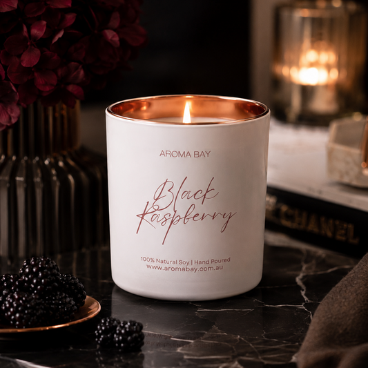 Aroma Bay Black Raspberry candle on a dark surface with flowers and another candle in the background.