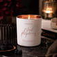 Aroma Bay Black Raspberry candle on a dark surface with flowers and another candle in the background.
