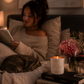 Woman reading a book in bed with a cat, candle, and wine glass on the nightstand.