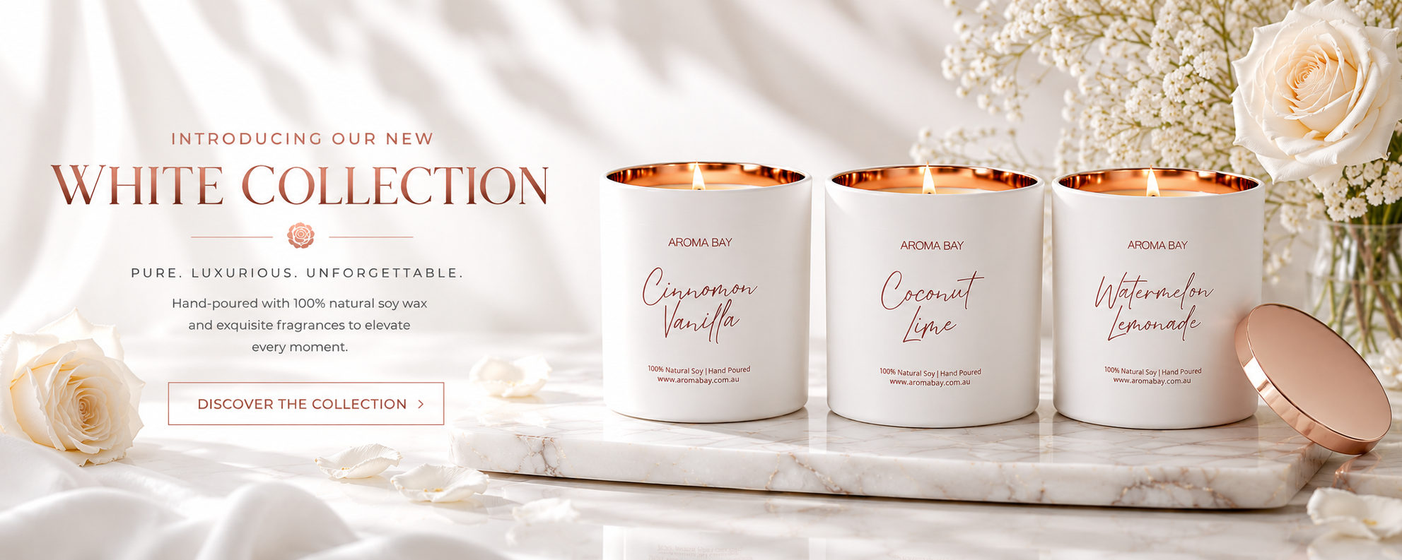 White candles with rose gold accents on a marble surface with white flowers and soft lighting.