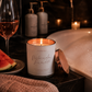 Candle labeled 'Watermelon Lemonade' next to a glass of wine and watermelon on a bathroom counter.