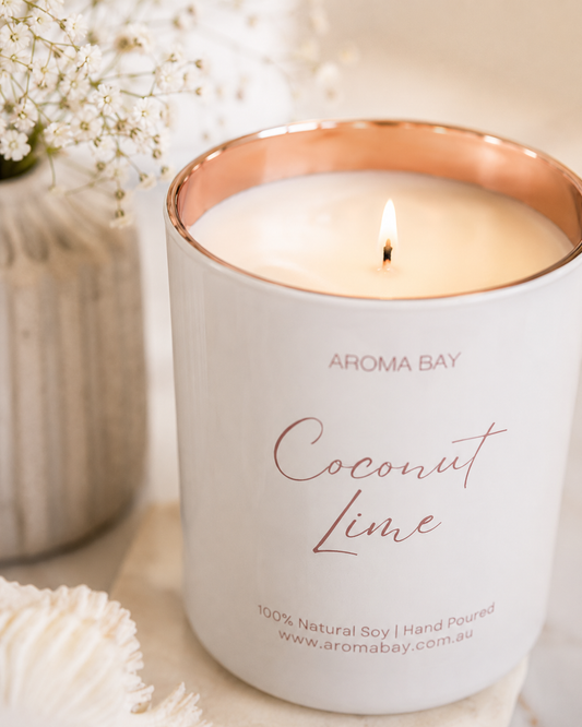 Aroma Bay coconut lime candle with a rose gold lid on a white surface with flowers in the background
