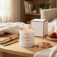 Candle labeled 'Strawberry Cream' on a wooden table with a cozy indoor setting.