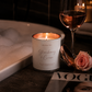 Candle labeled 'Strawberry & Cream' next to a glass of wine and a rose on a magazine with a blurred background.