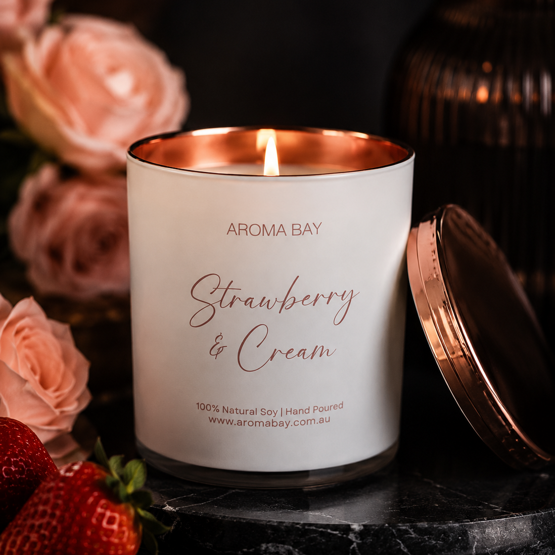 Aroma Bay Strawberry & Cream candle with roses and strawberries on a dark surface